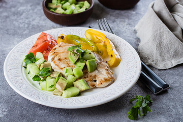 Grilled chicken breast with tomato and pepper grill and salsa from avocado and cucumber on plate on stone gray table background. Healthy Clean Diet Dinner Concept