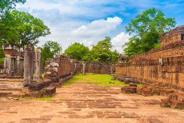 Fototapeta na wymiar The walkway on the first level of Cambodia's East Mebon temple. On the left are gallery ruins and on the right is the wall of the second level with a guardian elephant statue on the top corner.