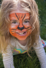 Close-up emotional portrait of a little girl with tiger aqua makeup, smiling and sitting in a park.