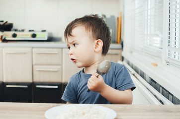 The little boy in the kitchen eagerly eating rice with a spoon independently