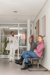 Patienten warten im Warteraum einer Arztpraxis, Arzt im Hintergrund