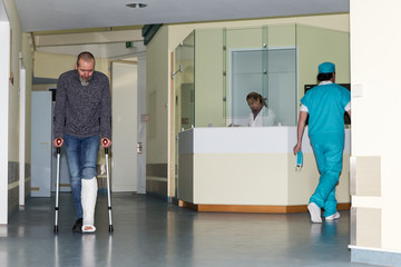 Patient mit Beinbruch und Krücken, Chirurg und Schwester im Korridor