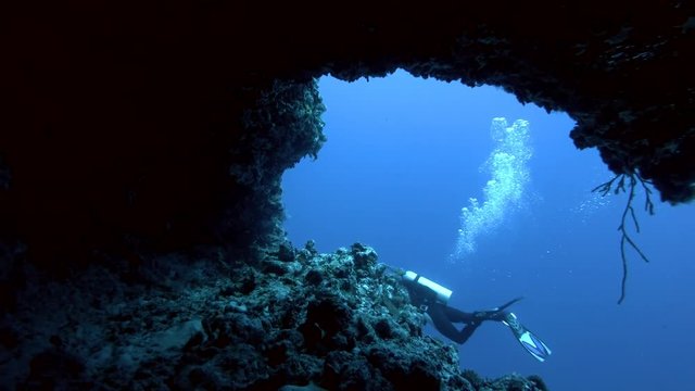 Young beautiful woman scuba swims near cave, Indian Ocean, Maldives
