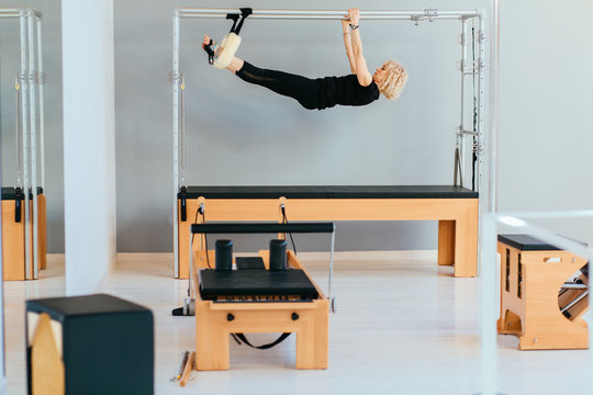 Elderly Female Blond Pilates Instructor Working Out On Cadillac In Eco Modern Inerior Pilates Studio. Health And Rehabilitation Concept. Sport Woman In Black Sportswear Gym Coach Fitness Exercise.