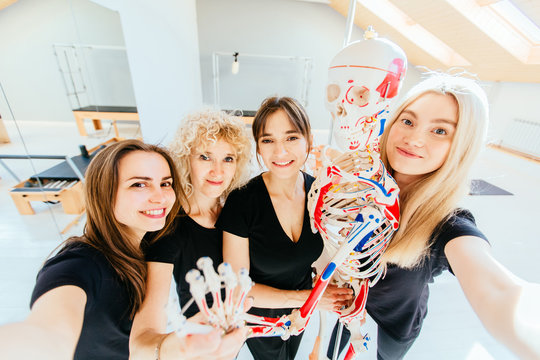 Group of four sporty multiracial friends taking selfie photo with skeleton smiling, hugging, looking at camera, happy healthy diverse fit people relaxing after working out together in pilates studio.
