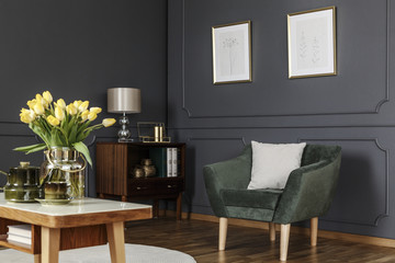 Green armchair against grey wall with posters in modern living room interior with flowers