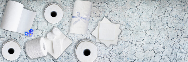 Paper tissue, white toilet  paper rolls, towels, napkins, cotton pads stacked on old gray marble table. Top view. Copy space. Wide panoramic image.