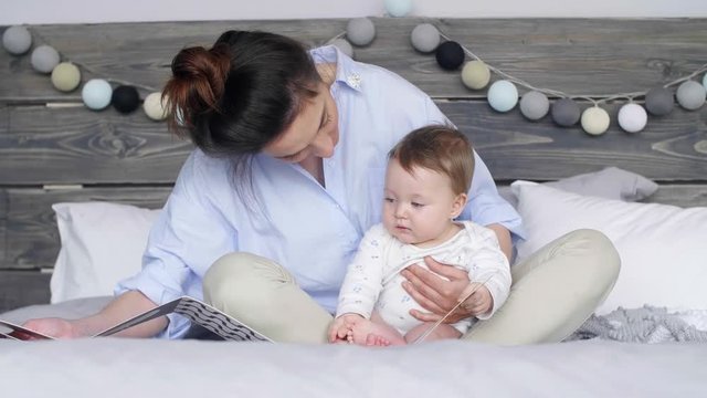 Mother and baby girl watching a picture book on bed