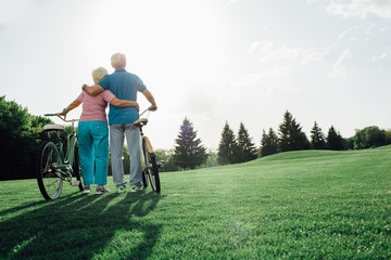 Senior couple with their bicycles standing and hugging, rear view. Active rest of the elderly people