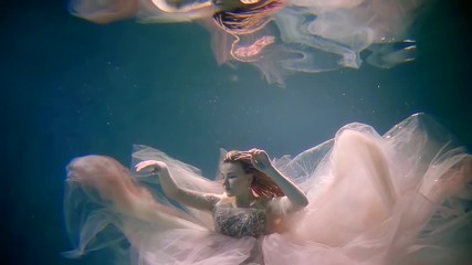 beautiful romantic bride is swimming underwater in pool and her reflection in surface is above her