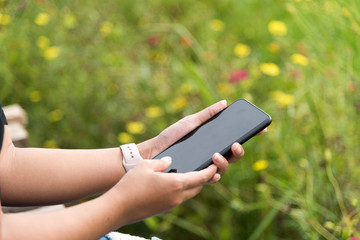 Asian woman wearing smartwatch and using smartphone in her vacation time at green field in selective focus.