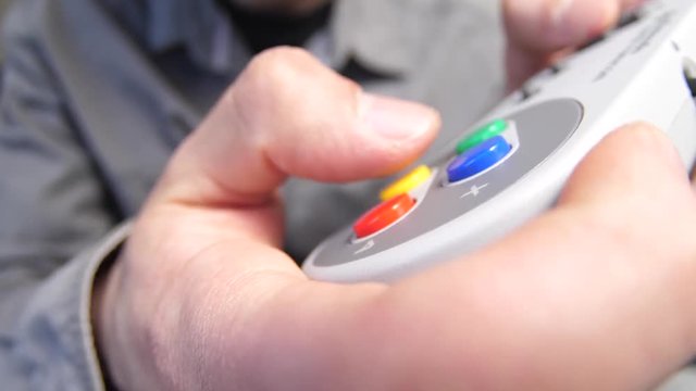 Closeup of hands playing on a retro gaming console controller, pressing the buttons.
