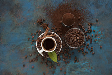 Сoffee in white cup сoffee beans and ground powder on brown background. Top view