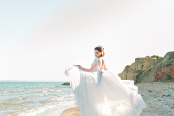 Fototapeta na wymiar Beautiful bride in luxury wedding dress with bouquet at the sea side. Wedding by the sea. Bride walking around the sea, standing back to camera.