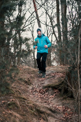 Fototapeta na wymiar Young man running outdoors during workout in a forest among leafless trees on cold freeze autumn day