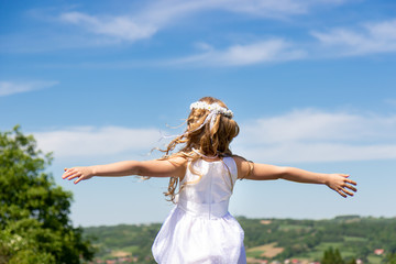 First Holy Communion, girl in white dress and wreath, blue sky in the background