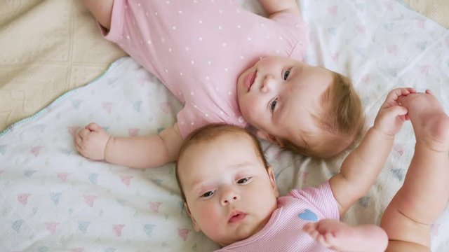 girls twin sisters in pink clothes lying on the bed