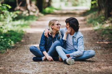 Romantic young couple sitting together in forest and enjoying sunny day together