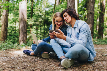 Fototapeta premium Young couple using laptop and tablet while sitting in forest