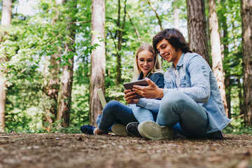 Young couple using laptop and tablet while sitting in forest