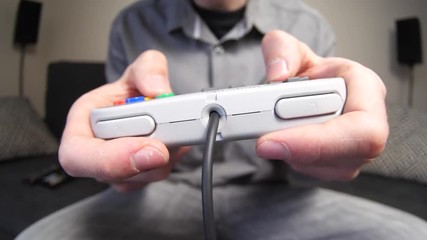 Closeup of hands playing on a retro gaming console controller, pressing the buttons.
