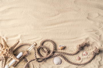 Fototapeta na wymiar Bottle with letter and shells with rope on light sand