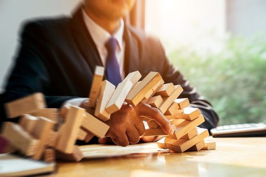 An asian businessman arraging the small wooden blocks on his working desk by close-up, Business construction and fail concept.