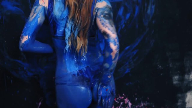 Seductive young woman eroticly dancing all in blue paint. Beautiful body