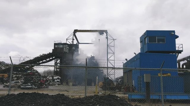 Recycling center machinery crushing the metal in many pieces. Smoke coming out. Car scrap