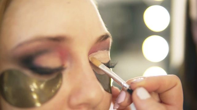 Make-up artist putting on light eyes shadows on model's eye. Close up. Patches. Side view
