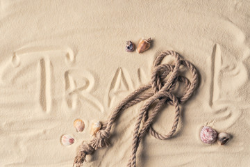 Fototapeta na wymiar Rope and shells on sandy beach with rope and Travel inscription