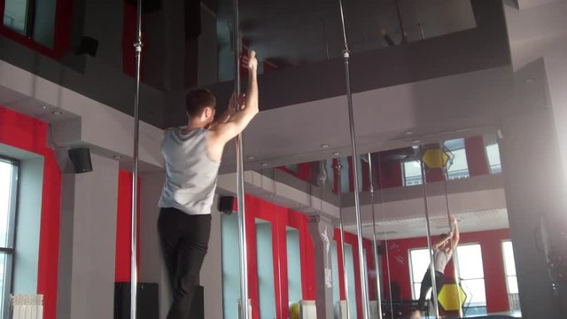 Athletic young man performing pole dance exercises in a studio