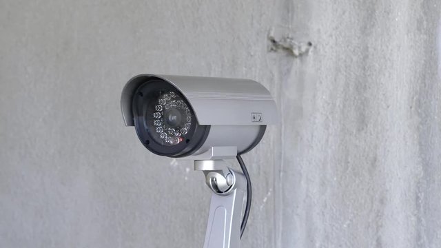 Security camera moving panning and tilting recording what's happening outside a building. Motorized CCTV surveillance.