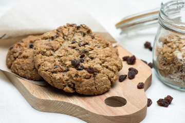 Oatmeal cookie with raisins lying on wooden board next to the jar.