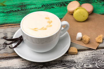Vanilla cappuccino in a white cup with sugar and macaroons on wooden table