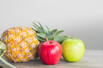 Ripe pineapple red apple and green apple on wooden table.many fruit for health.