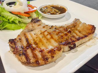 Grilled pork chop steak with salad and sauce in a white plate .