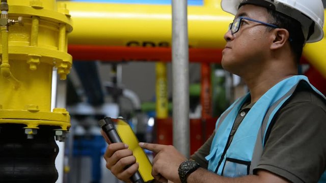 Asian engineer wearing glasses working in the boiler room,maintenance checking technical data of heating system equipment,Thailand people