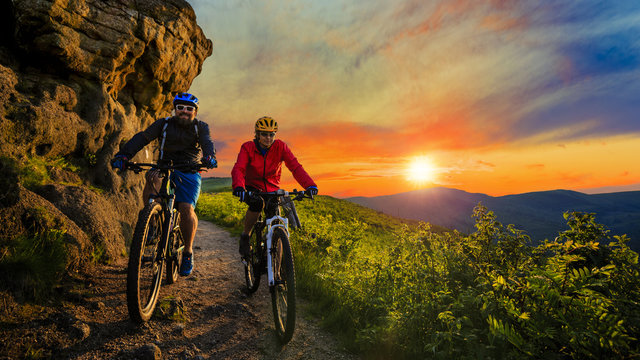 Cycling woman and man riding on bikes at sunset mountains forest landscape. Couple cycling MTB enduro flow trail track. Outdoor sport activity.