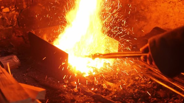 Hands of blacksmith using tongs to help him smelt down metal