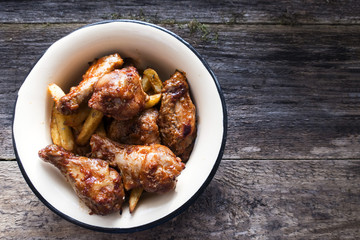 Appetizing chicken pieces and french fries with seasoning in a beautiful old bowl and on an old wooden background and copy space