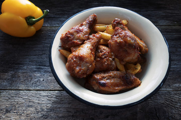 Appetizing chicken pieces and french fries with seasoning in a beautiful old bowl and on an old wooden background and yellow pepper