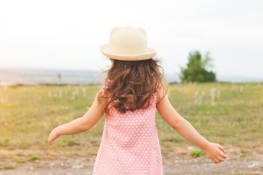 Little girl's back in hat and dress in summer field
