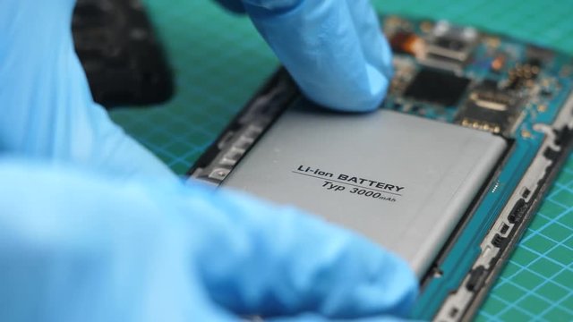 Replacing the internal battery of a smartphone mobile device. Closeup of the repair being done by a person wearing gloves.