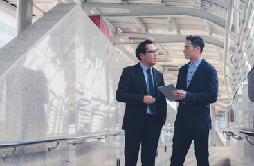 two attractive business man talking discussion and looking at tablet using touching pad with walking at outdoor walk way in city on morning.