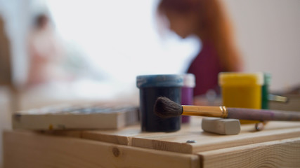 Art supplies and paints in front of painer performing artistic etude witn naked model