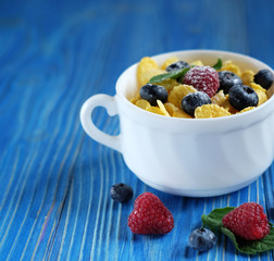Healthy eating, food and diet concept - Cornflakes with berries raspberries and blueberries on blue wooden background. Top view.