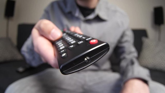 Young man sitting on his sofa zapping trough channels on his remote control. Filmed with a fisheye lens for a more dramatic effect.