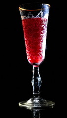 Illuminated patterned glass of red wine with gold shadow with reflection on black background