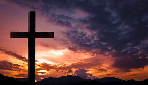Jesus Christ cross, wooden crucifix. Crucifixion concept on a heavenly background with dramatic light and clouds and colorful orange, purple sky at sunset. Religious Easter, resurrection concept